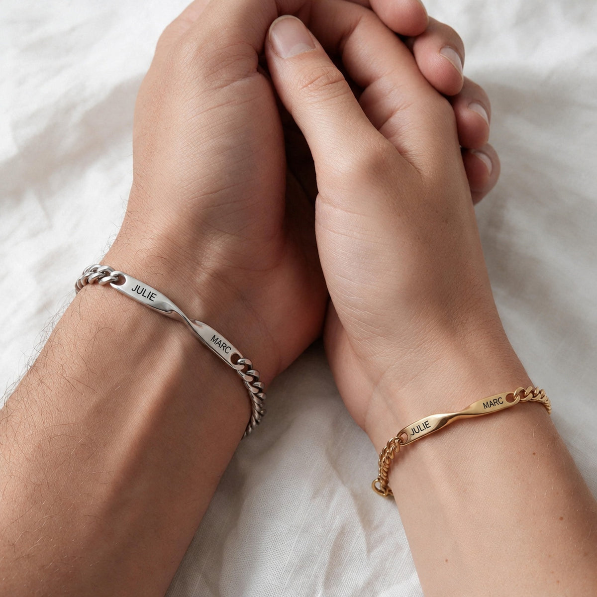 Couple main dans la main : lui bracelet argent, elle bracelet or, gravés JULIE · MARC